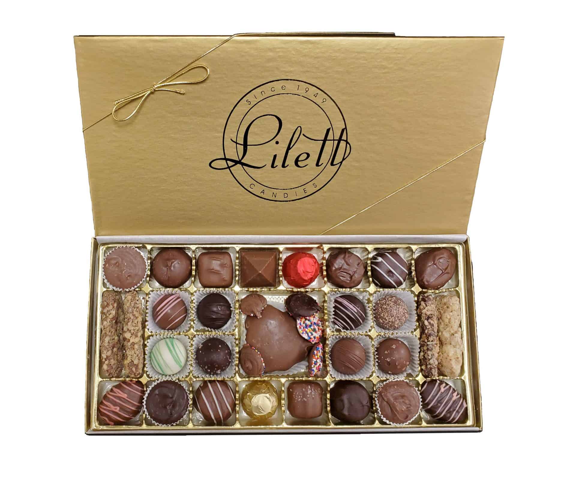 The Ultimate Holiday Sampler features an open gold box of assorted chocolates from Piletti Candies, arranged in neat rows with a variety of shapes, colors, and festive decorations.