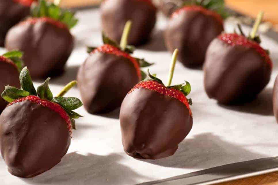 Several strawberries coated in chocolate are arranged on a parchment-lined baking sheet.