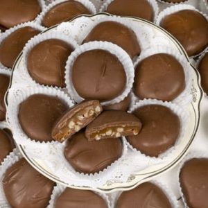 A plate of round chocolate-covered candies, some cut open to reveal a caramel and nut filling, arranged on white paper liners.