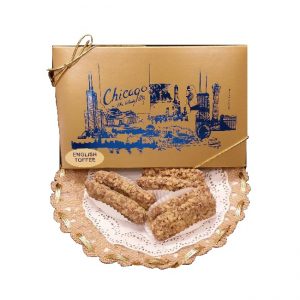 A gold box labeled "Chicago Toffee" with a city skyline design sits behind three pieces of English toffee on a lace doily.
