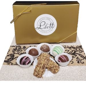 A gold gift box labeled "Lilett" with six assorted chocolate truffles and two nut-covered confections arranged in front on a patterned mat.