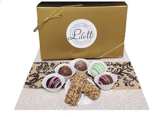 A gold gift box labeled "Lilett" with six assorted chocolate truffles and two nut-covered confections arranged in front on a patterned mat.