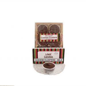 A box labeled "Lilett Candies Cashew Clusters - Milk" with six chocolate clusters inside and one unwrapped chocolate cluster displayed on a doily in front.
