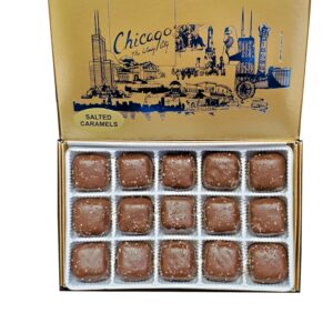 A gold box labeled "Chicago" contains sixteen salted caramel chocolates in individual wrappers, with an illustrated city skyline on the inside lid.