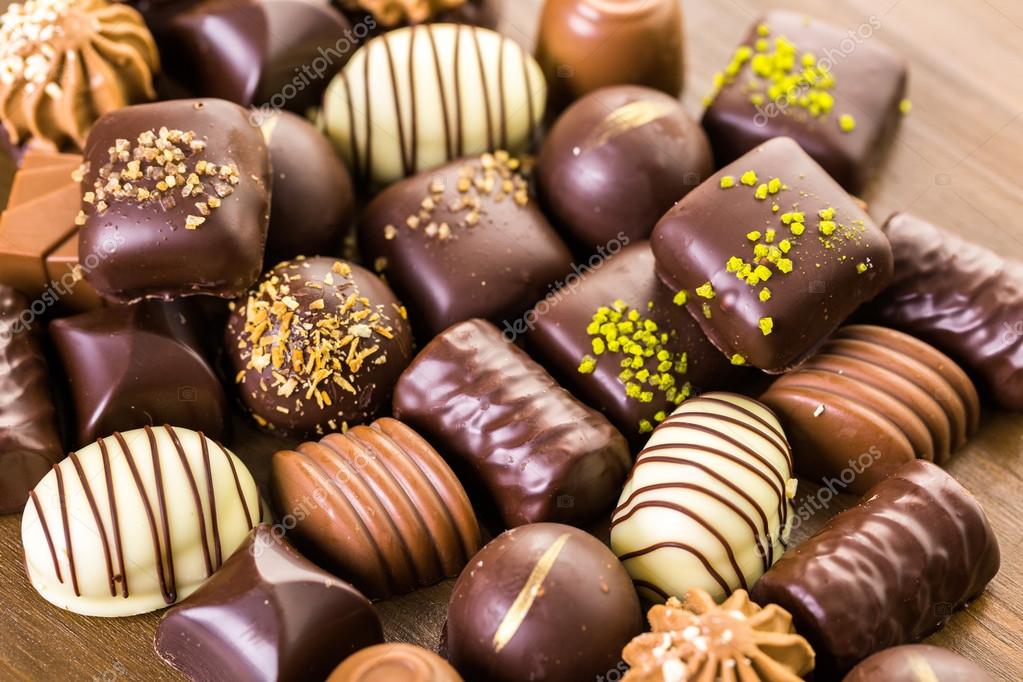 An assortment of various chocolate pralines and truffles with different toppings and decorations arranged on a wooden surface.